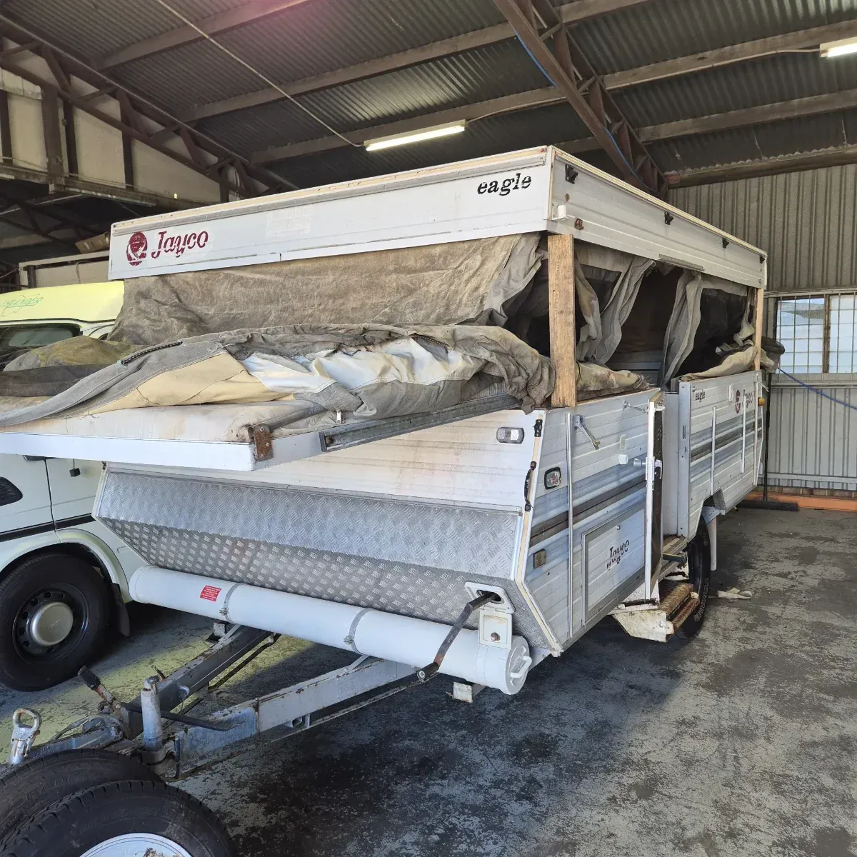 White and silver Jayco Eagle pop-up camper with partially open roof in a corrugated metal shed — Revive Caravan Repairs in Kippa-Ring, QLD