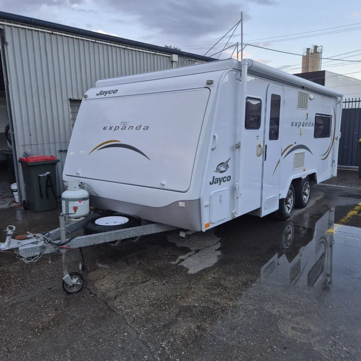 White Jayco Expanda caravan parked on a wet asphalt lot, with a cloudy sky in the background — Revive Caravan Repairs in Kippa-Ring, QLD