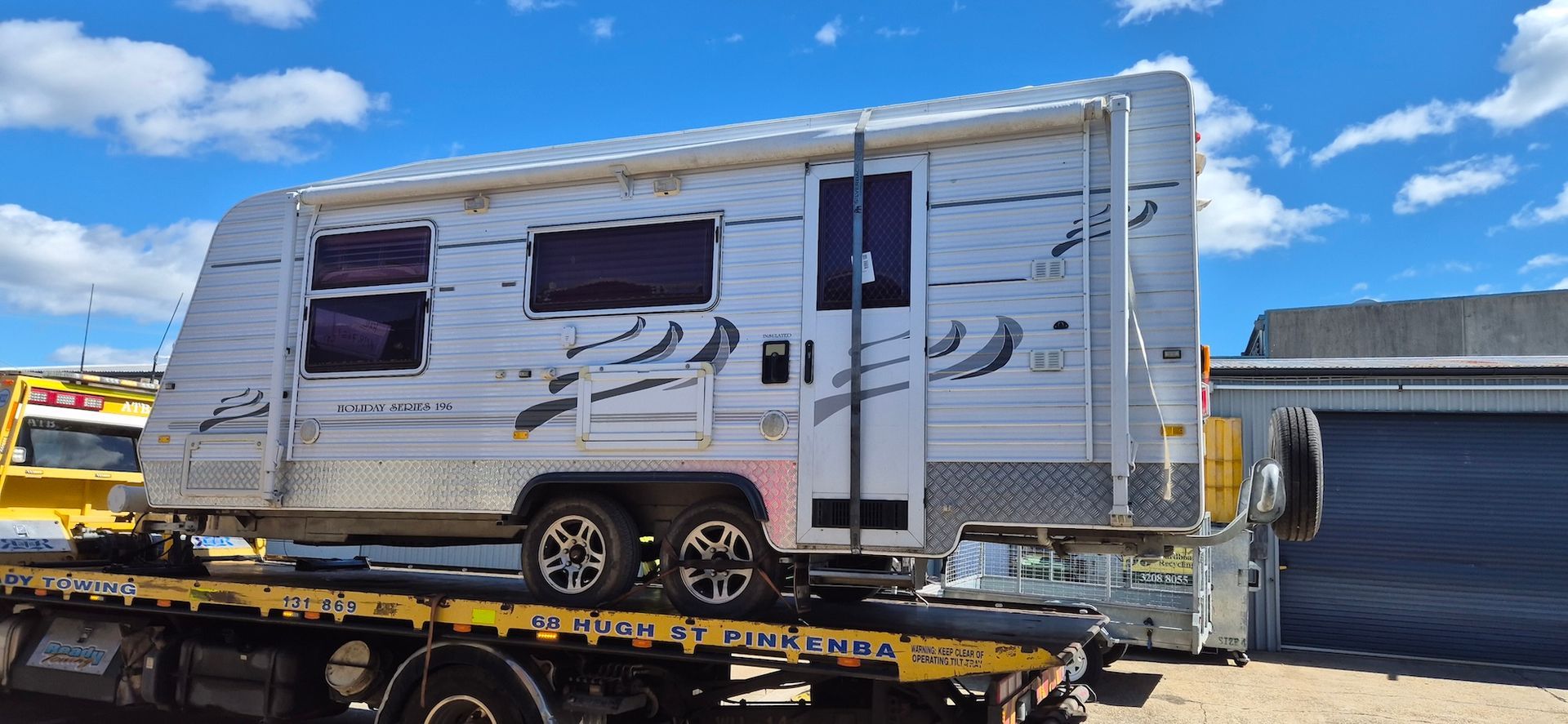 A caravan being transported on a flatbed truck against a blue sky— Revive Caravan Repairs in Brisbane, QLD