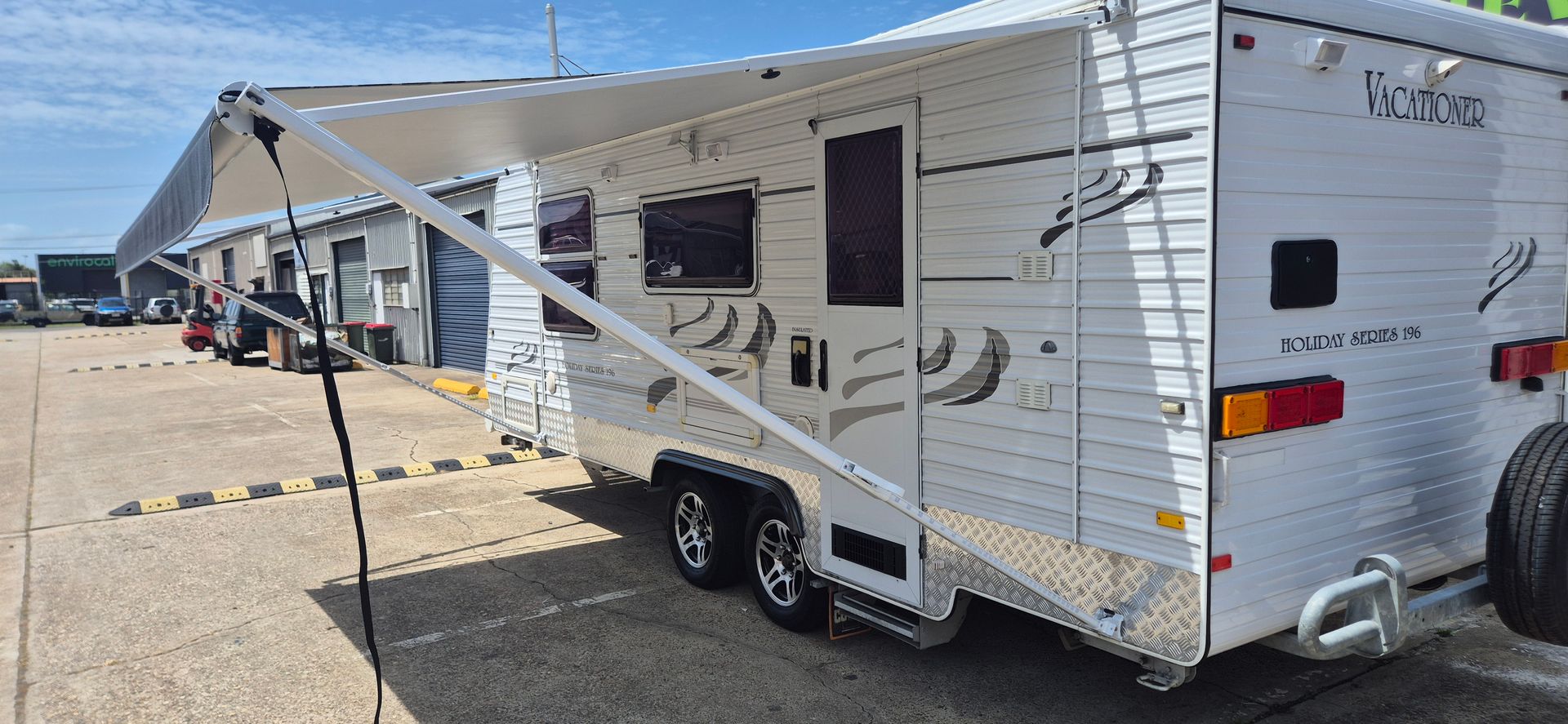 A Caravan with An Extended Awning Parked Outside a Building — Revive Caravan Repairs in Kippa-Ring, QLD
