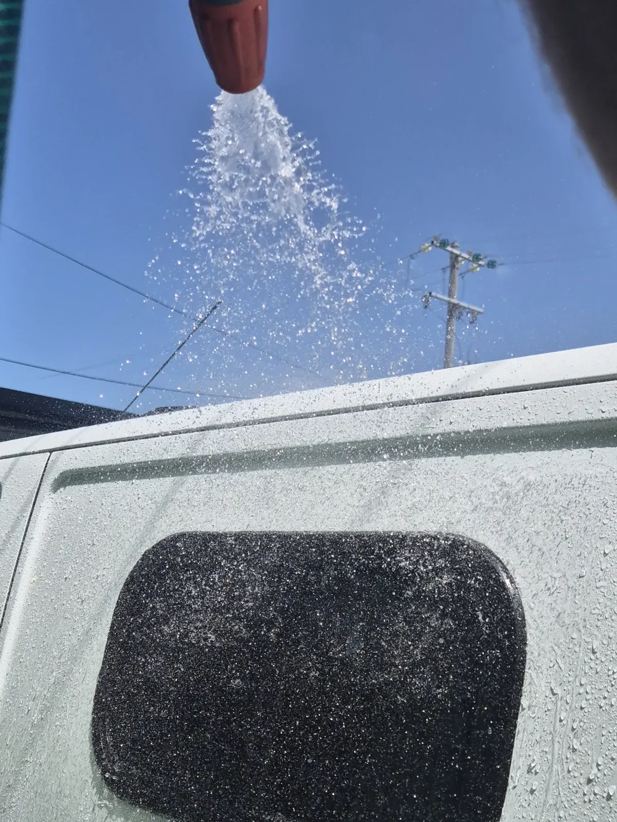 Water spraying from a red nozzle onto a white van, under a clear blue sky — Revive Caravan Repairs in Kippa-Ring, QLD