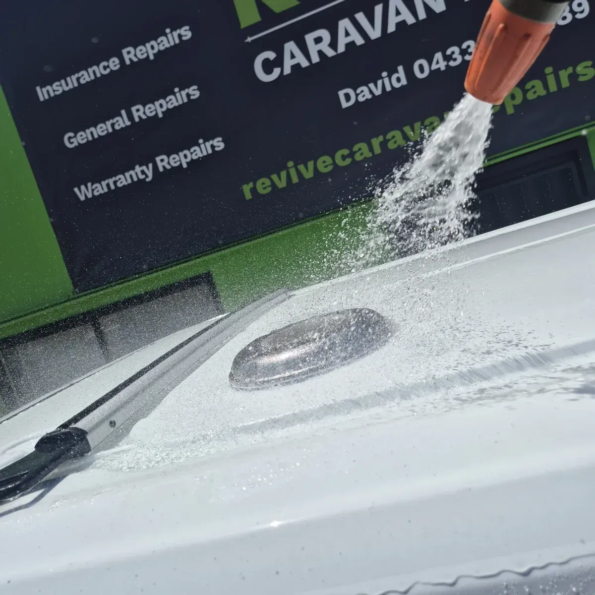 A white caravan being washed with a hose, near a sign — Revive Caravan Repairs in Kippa-Ring, QLD