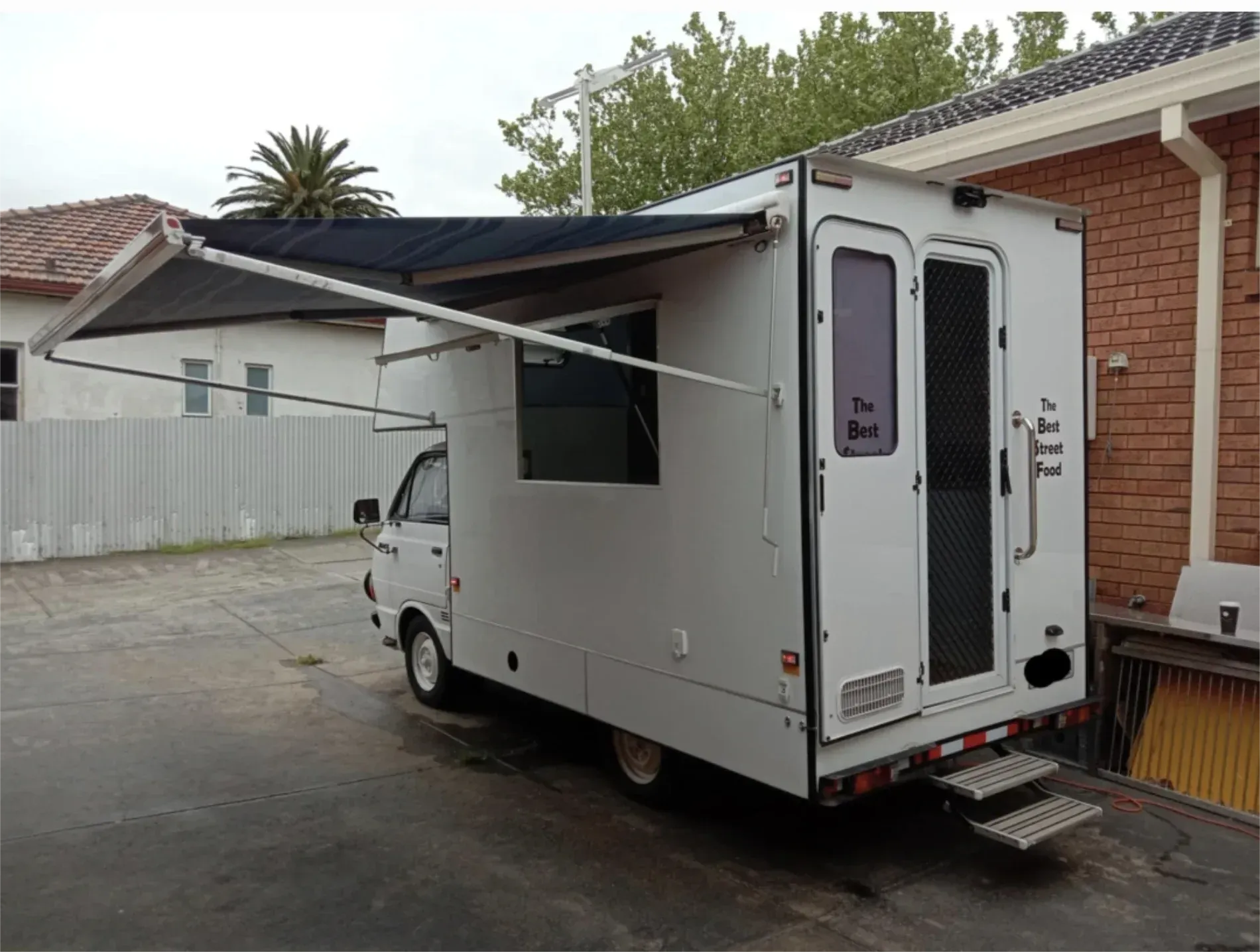 White campervan with an awning extended, parked near a brick building — Revive Caravan Repairs in Kippa-Ring, QLD