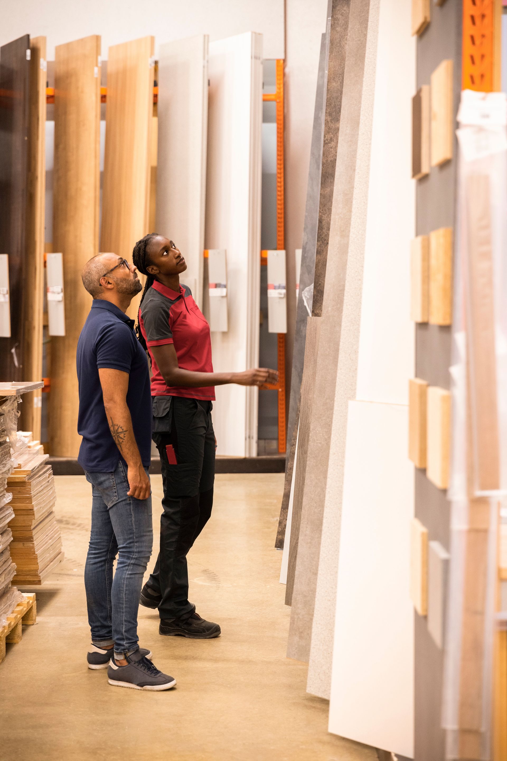Customer and sales staff looking up while selecting laminated boards at hardware store.