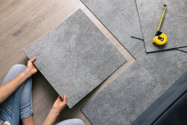 Woman laying carpet tiles on floor in living room.