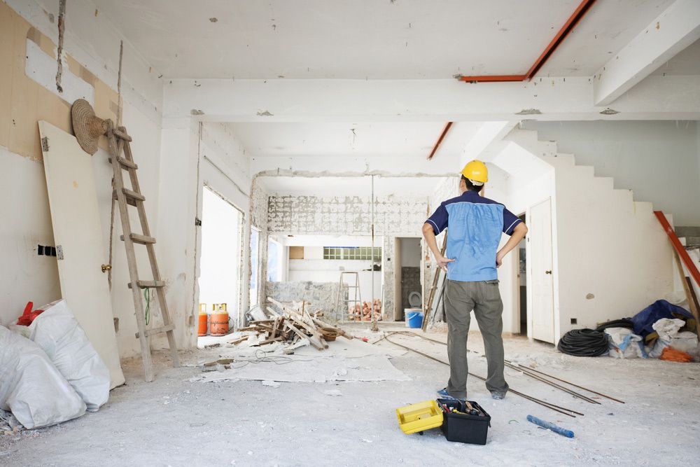 A Man In A Hard Hat Is Standing In A Room Under Construction — Renovation Electrician In Wagga Wagga, NSW