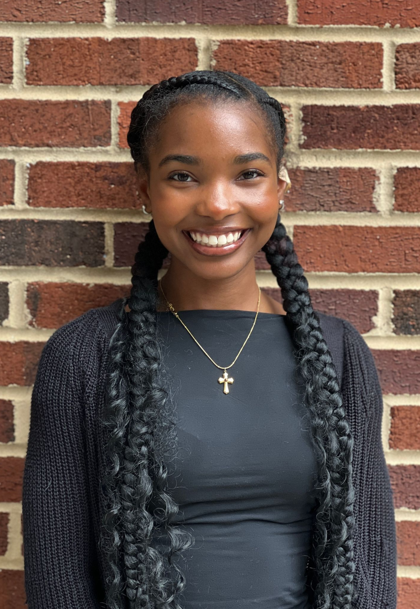 A woman in a black scrub top is smiling in front of a brick wall.
