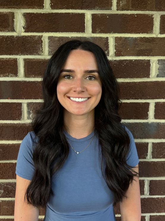 A woman with long red hair is smiling in front of a brick wall.