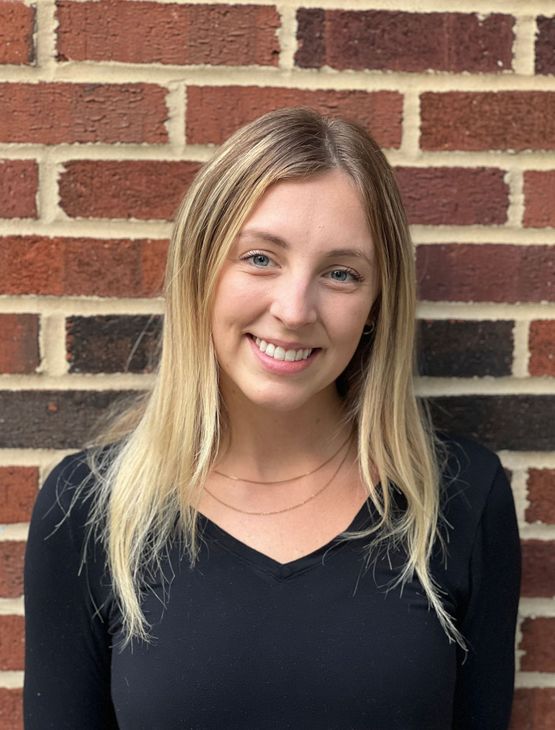 A woman in a black shirt is smiling in front of a brick wall.