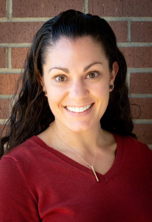 A woman in a red shirt is smiling in front of a brick wall