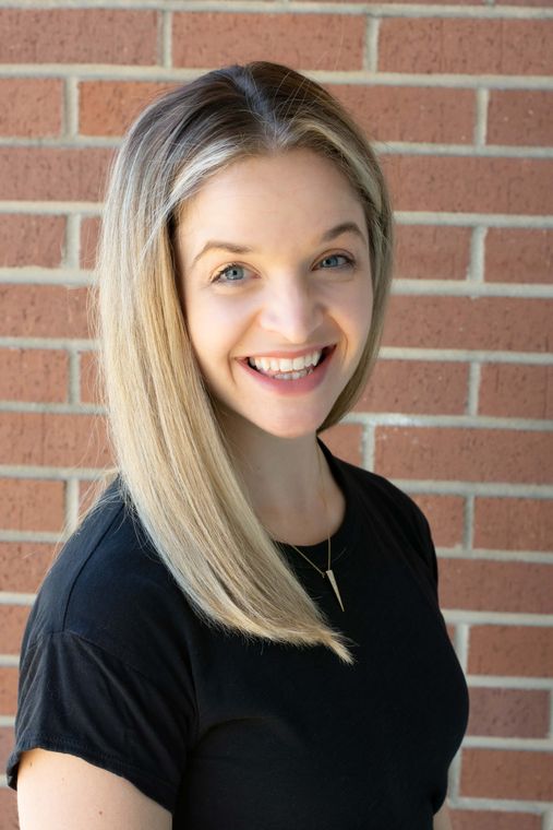 A woman in a black shirt is smiling in front of a brick wall.