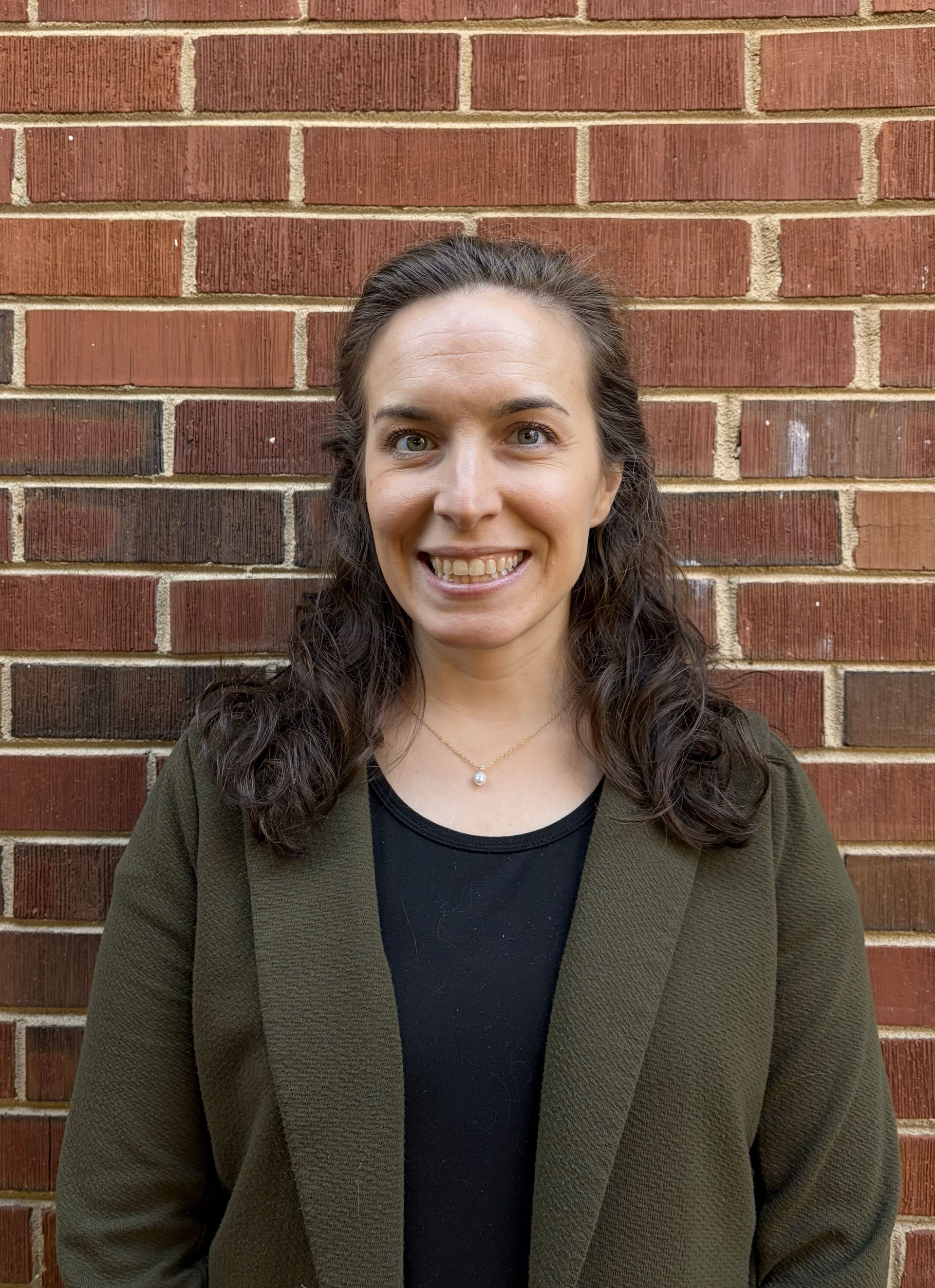 A woman with long red hair is smiling in front of a brick wall.