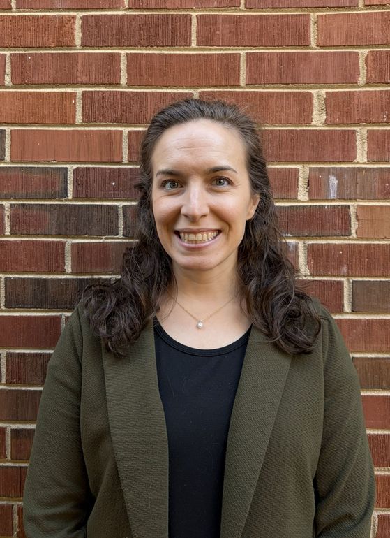 A woman with long red hair is smiling in front of a brick wall.
