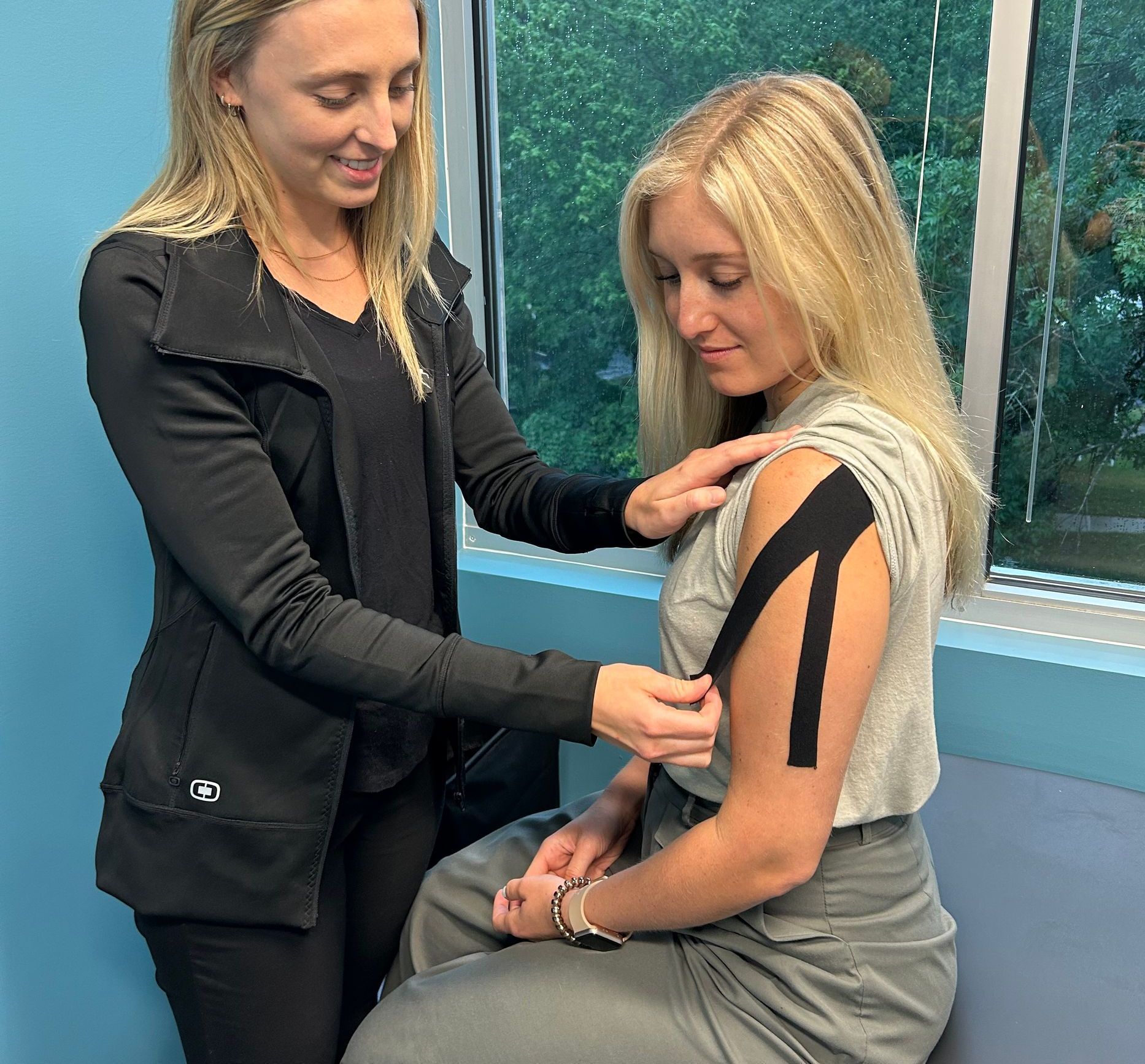 A woman is putting tape on another woman 's arm