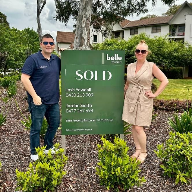A Man and Woman Standing Next to a Sold Sign — Hyde Burchell Buyers Agents In Canberra, ACT