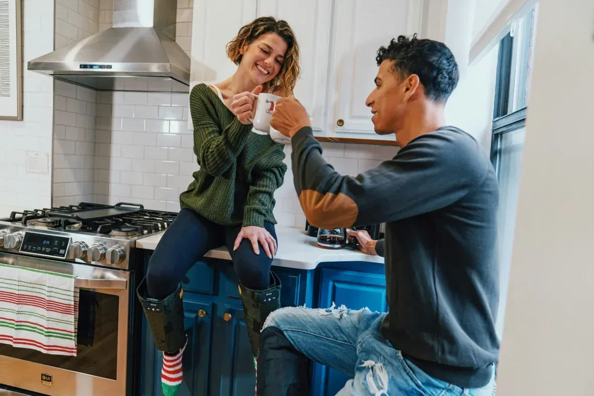 A Man and a Woman Are Sitting on a Kitchen Counter Drinking Coffee — Hyde Burchell Buyers Agents In Canberra, ACT