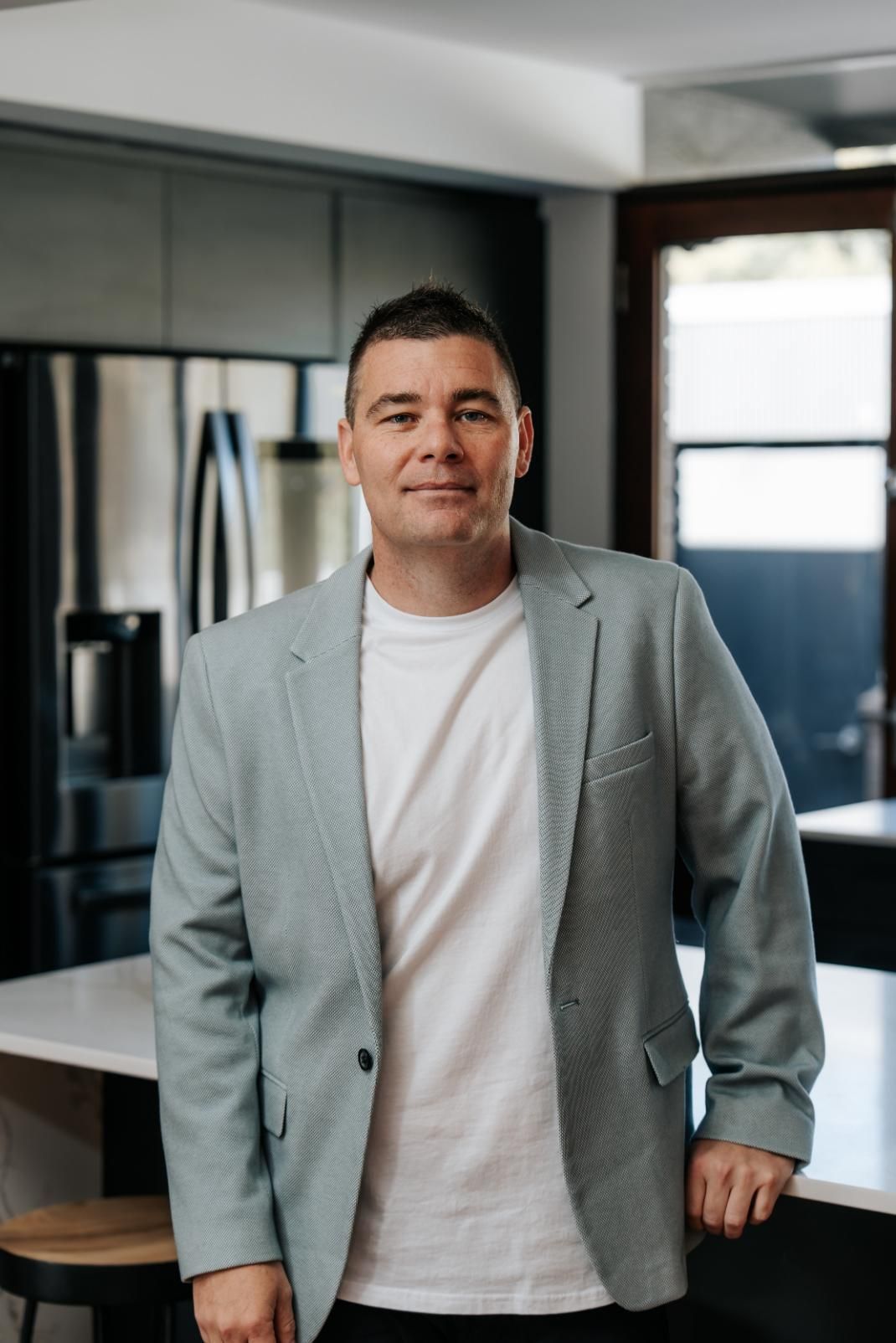 A Man in a Suit and White Shirt is Standing Next in a Kitchen — Hyde Burchell Buyers Agents In Canberra, ACT