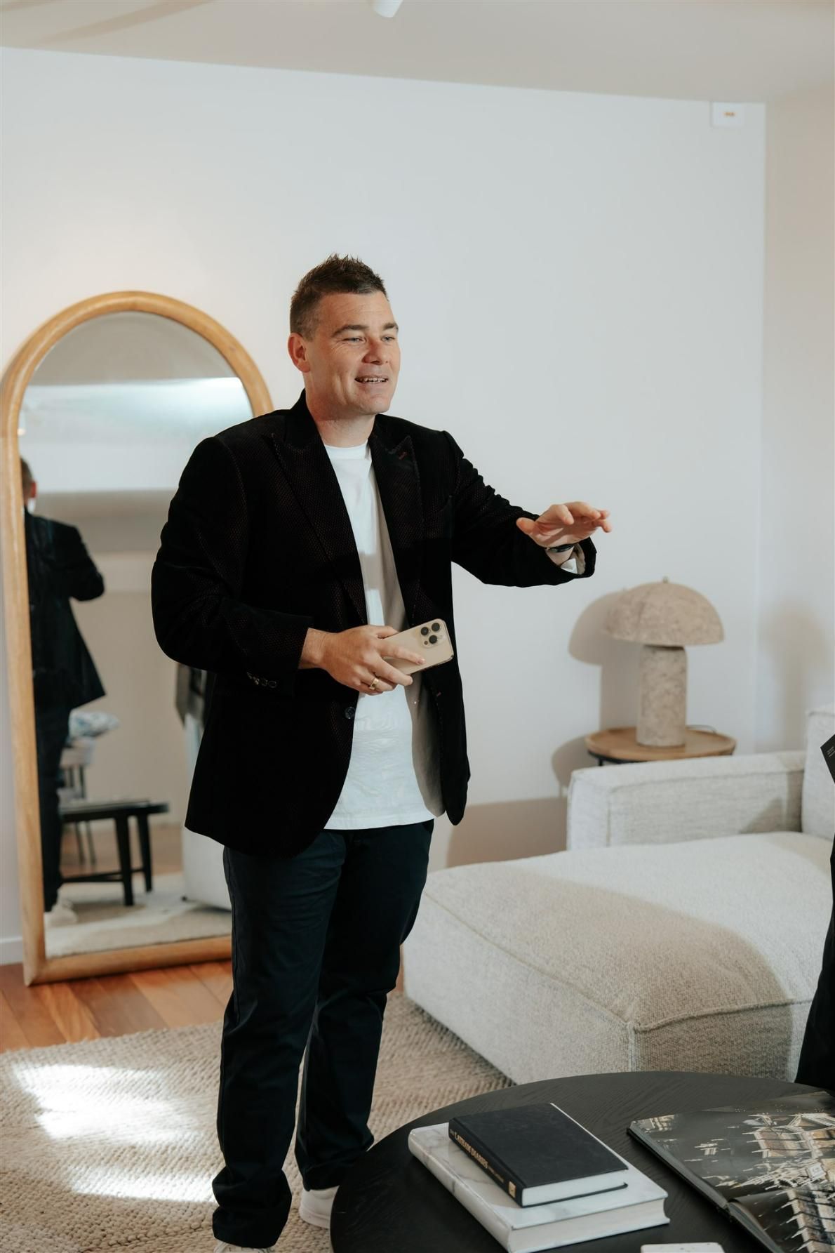 A Man in a Black Jacket is Standing in a Living Room Holding a Cell Phone — Hyde Burchell Buyers Agents In Canberra, ACT