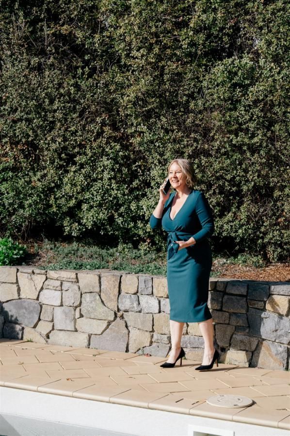 A Woman in a Green Dress is Talking on a Cell Phone — Hyde Burchell Buyers Agents In Canberra, ACT