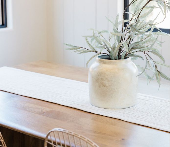 A White Vase With a Plant in It Sits on a Wooden Table — Hyde Burchell Buyers Agents In Canberra, AC