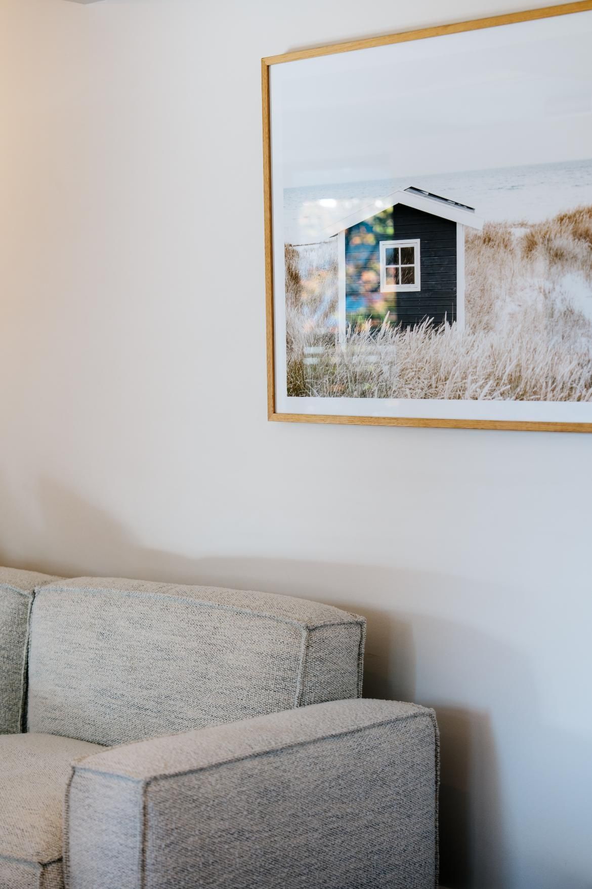 Off-white Couch Beneath a Framed Photo of a Small, Dark Building Surrounded by Tall Grass — Hyde Burchell Buyers Agents In Canberra, ACT