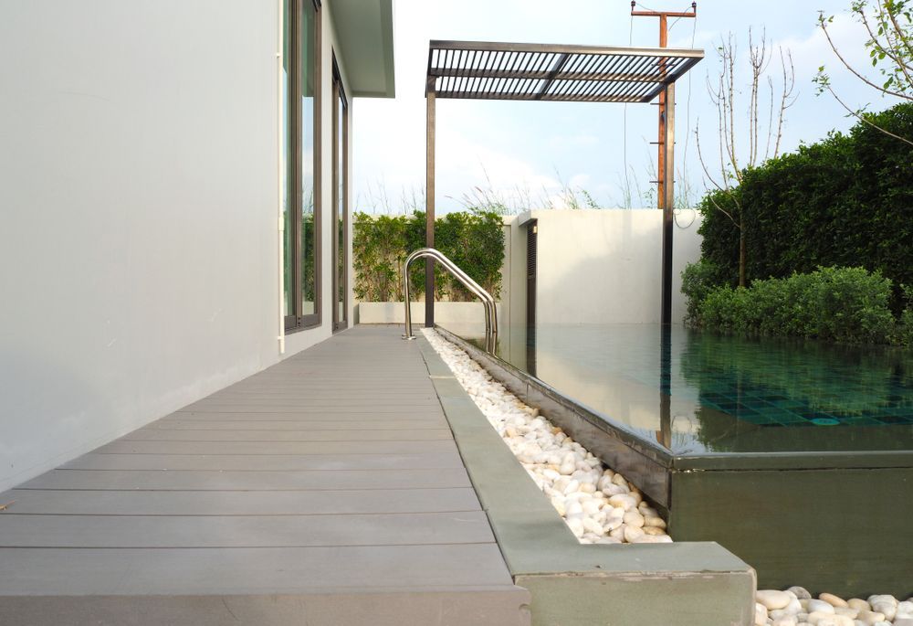 Poolside View: Gray Deck, Small White Stones, Rectangular Pool, Stainless Steel Shower, Light-colored House Wall, Green Hedge — Hyde Burchell Buyers Agents In Canberra, ACT