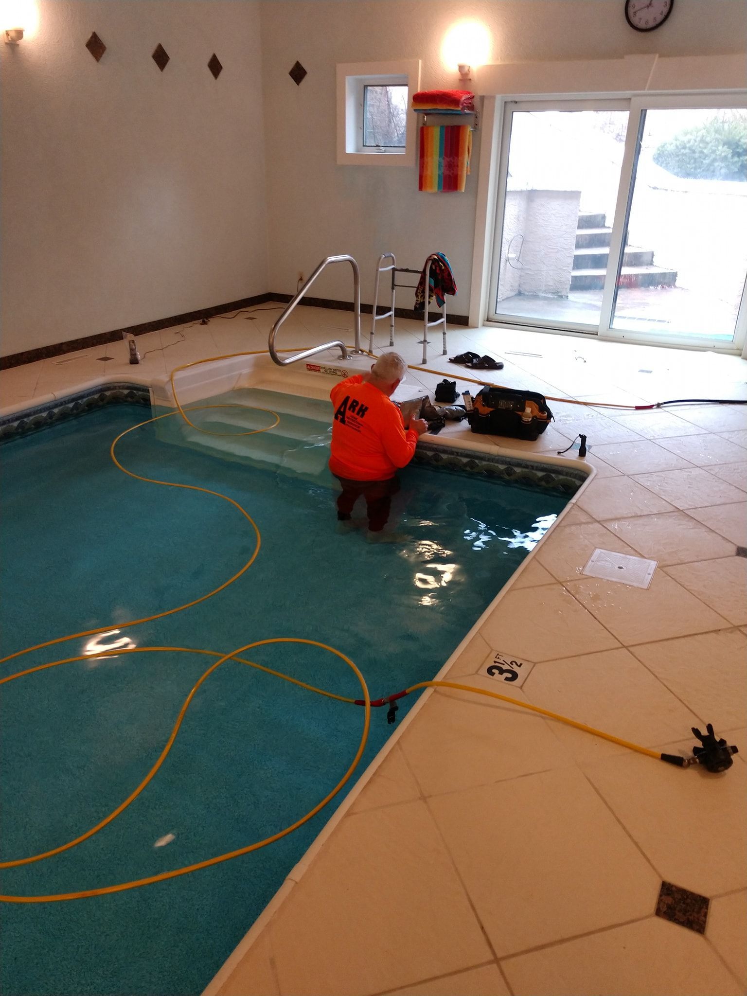 A man in an orange shirt is working on a swimming pool.