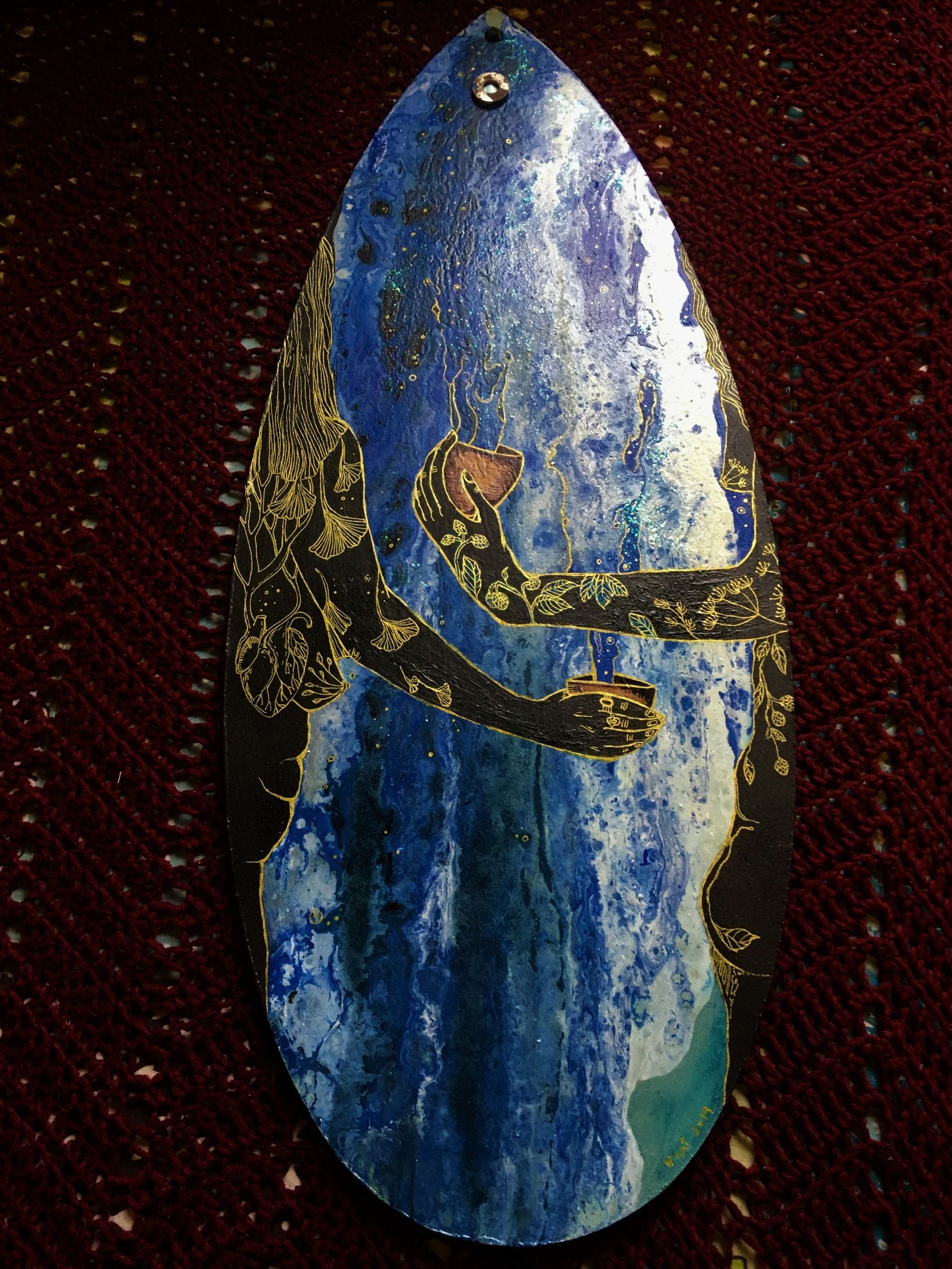 Painting of a blue paint pout on an interesting tear drop shaped canvass I found discarded in the woods on a dog walk. Two woman are seen, holding their glasses up to receive some of this blue energy. They are both painted black with gold tattoos of plants, leaves and medicine.