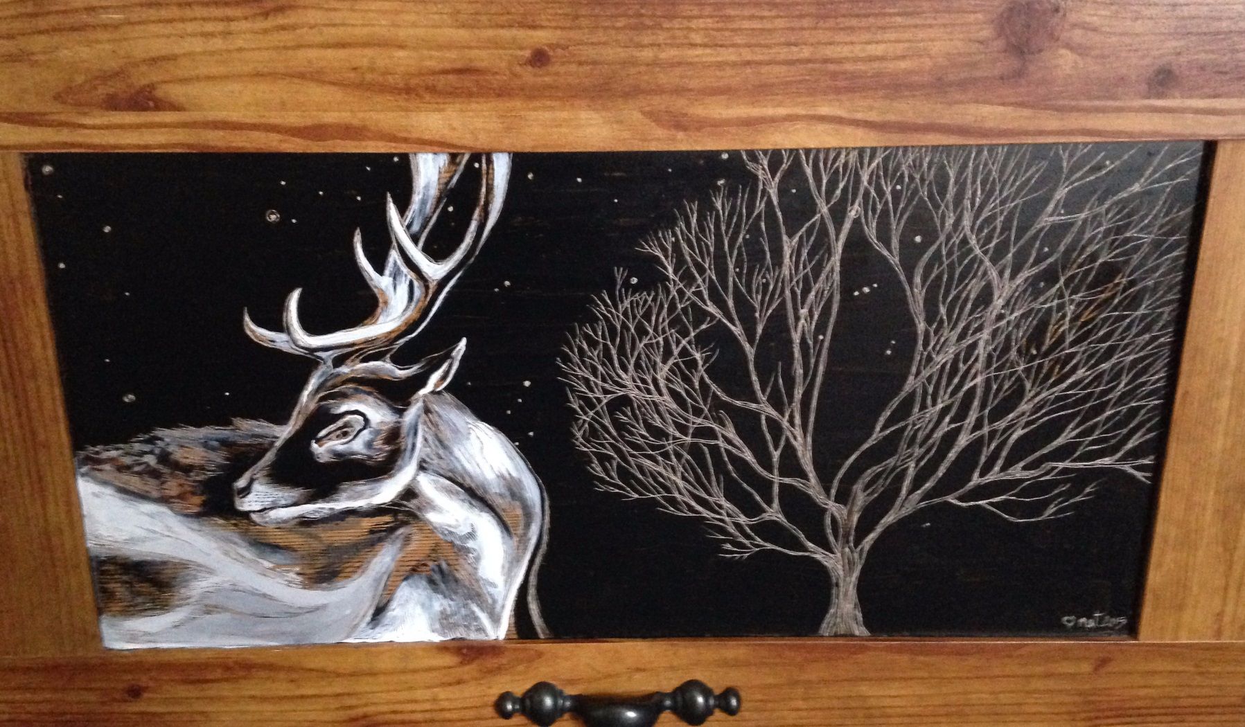 Painting of a deer-buck etched into a black background with a tree to the right of it also etched into black. The canvass is a large cupboard door with a pretty handle I found in the garbage and spruced up.