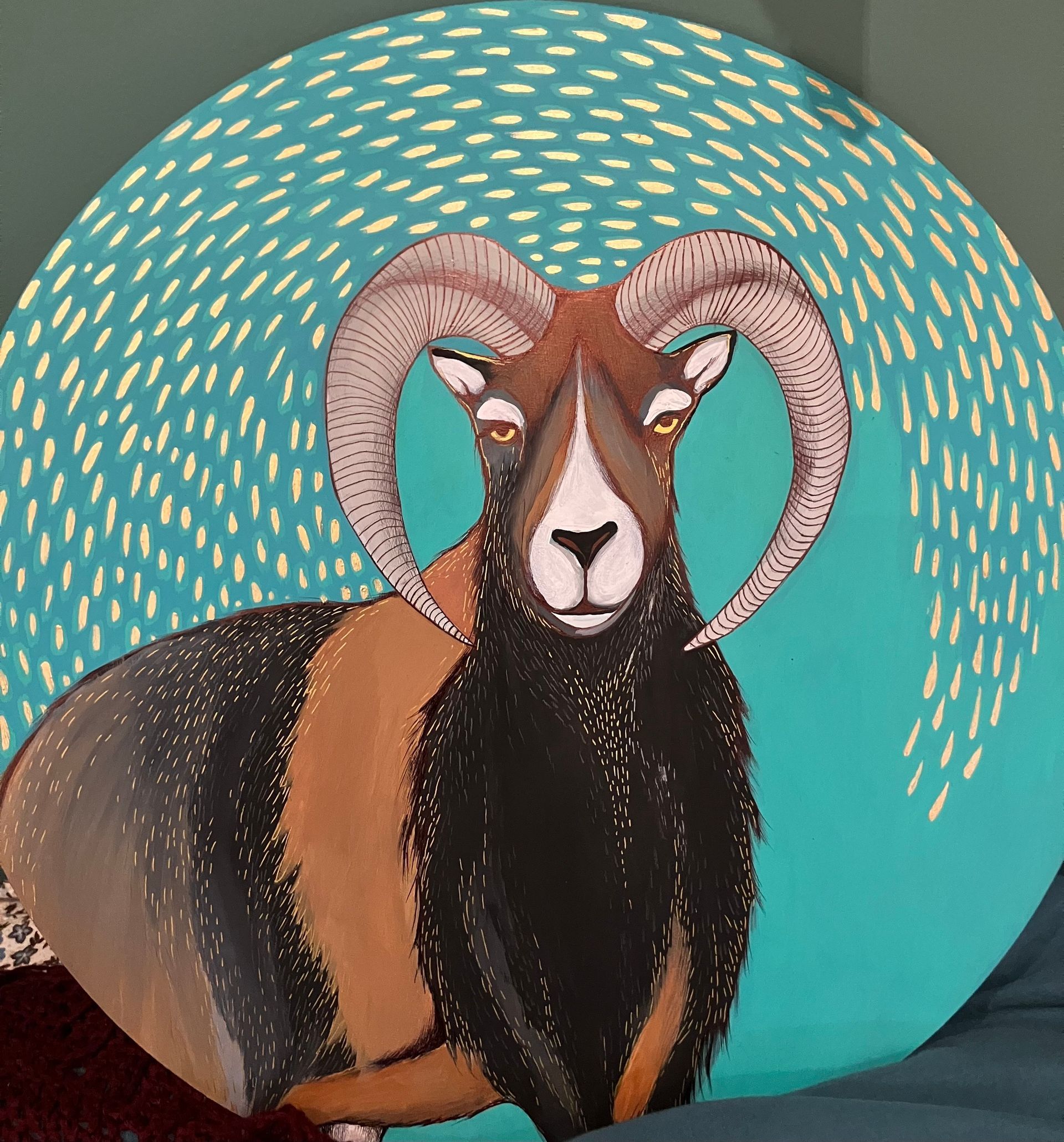 Image of a black and brown Ram painted on round wood, with acrylic ink on a blew background, raining sold from left to right.