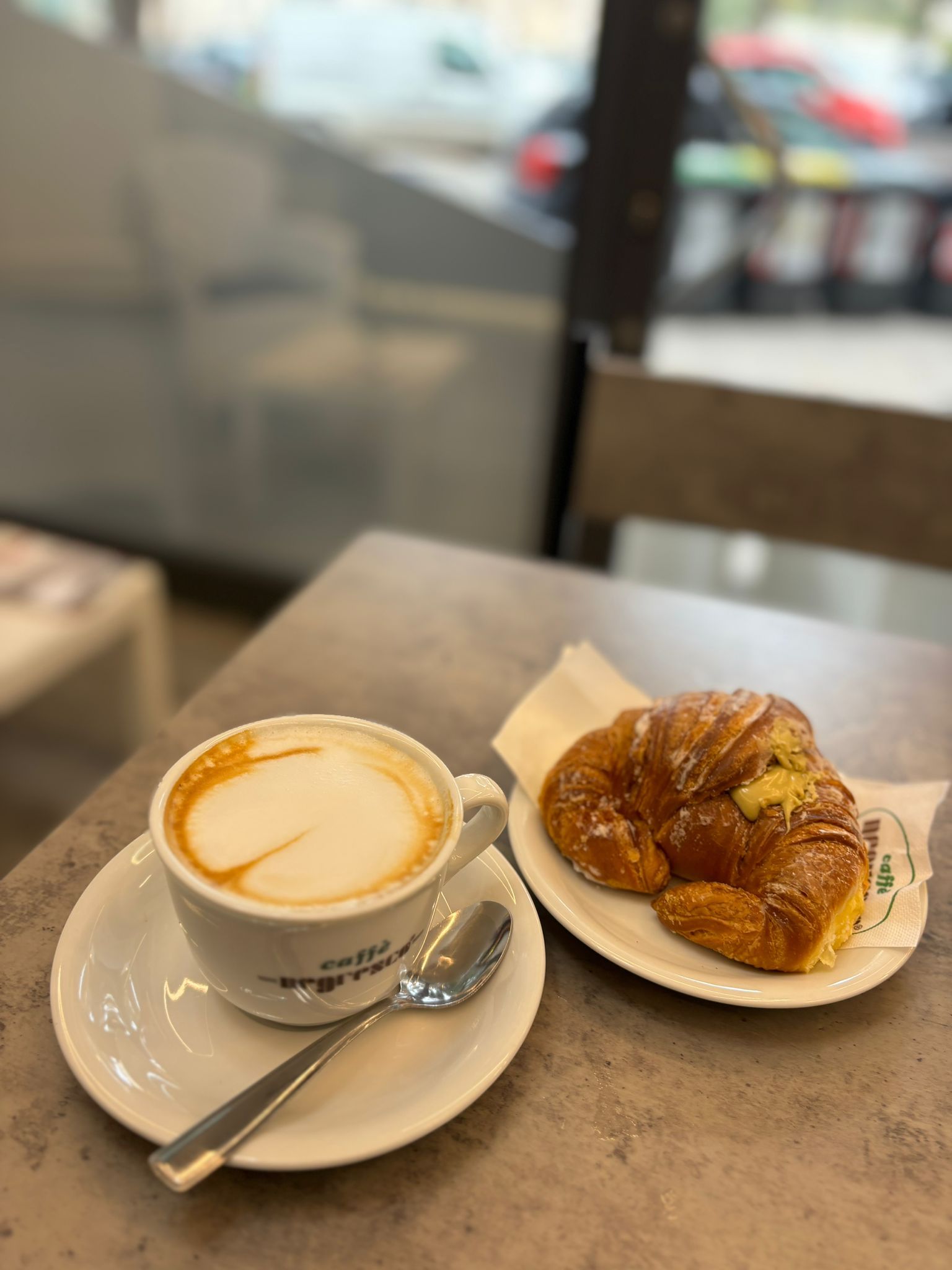Su un tavolo ci sono una tazza di caffè e un cornetto.