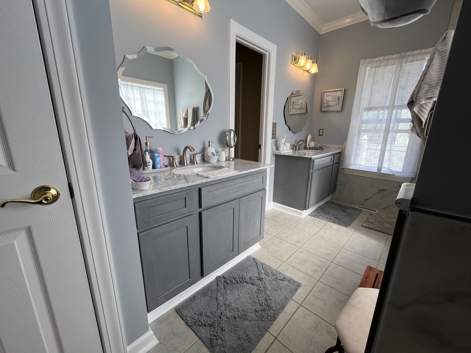 Bathroom with two gray vanities, decorative mirrors, and a window. Light gray walls and tile floor.