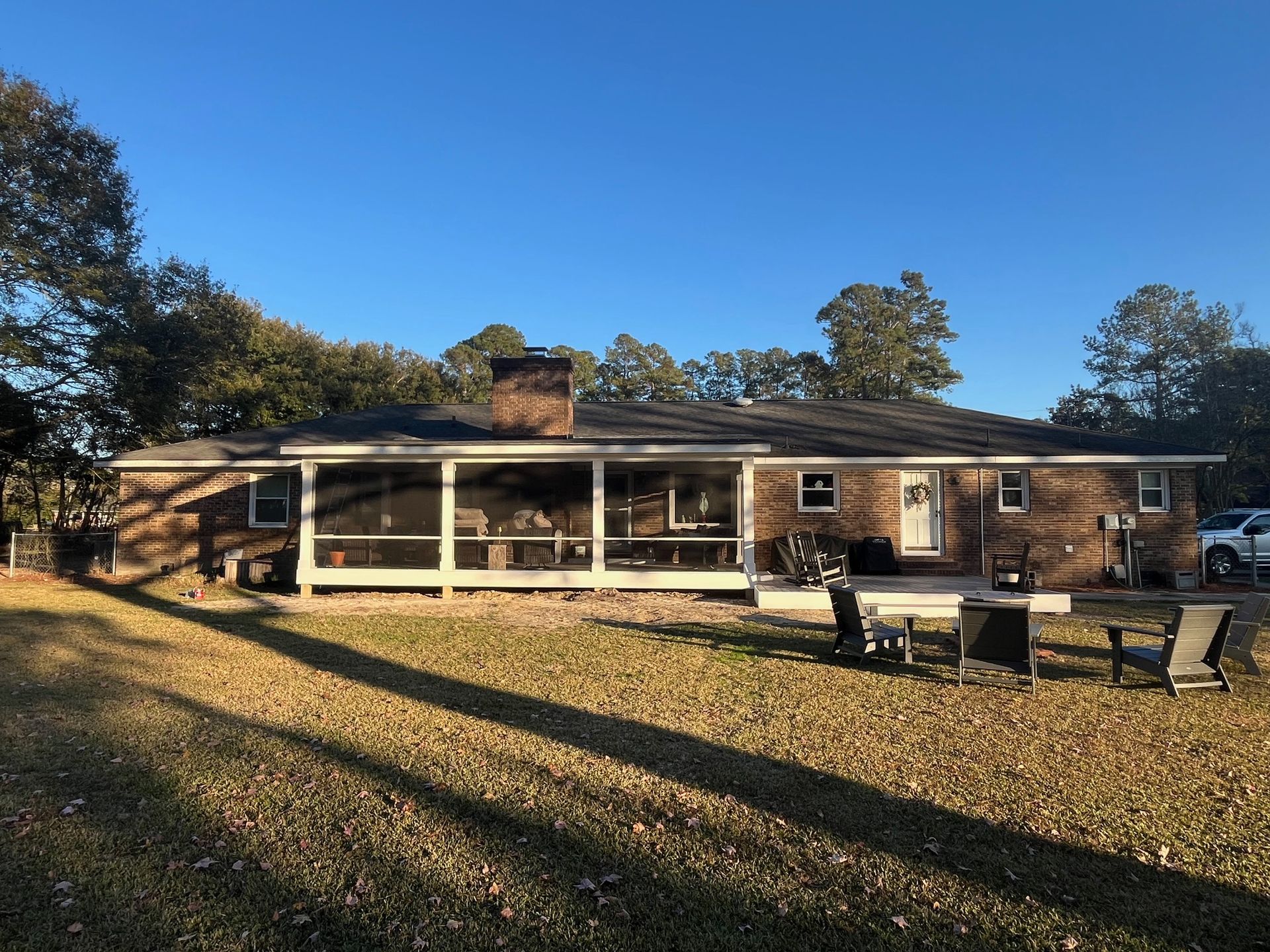 Screened porch attached to a brick house with outdoor seating and steps. Green grass and blue sky.