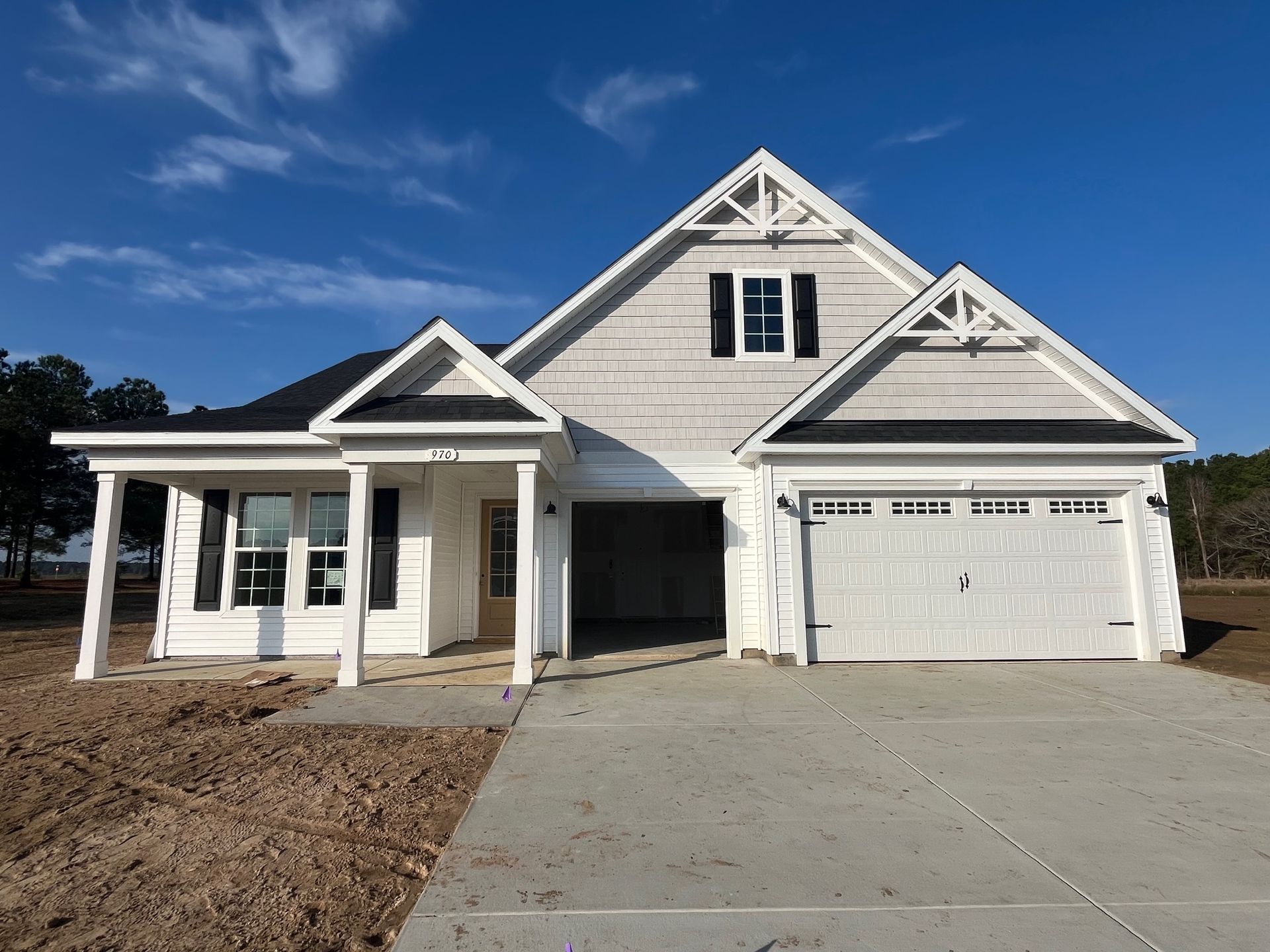 White house with a gabled roof and attached garage, on a concrete driveway. Clear blue sky.