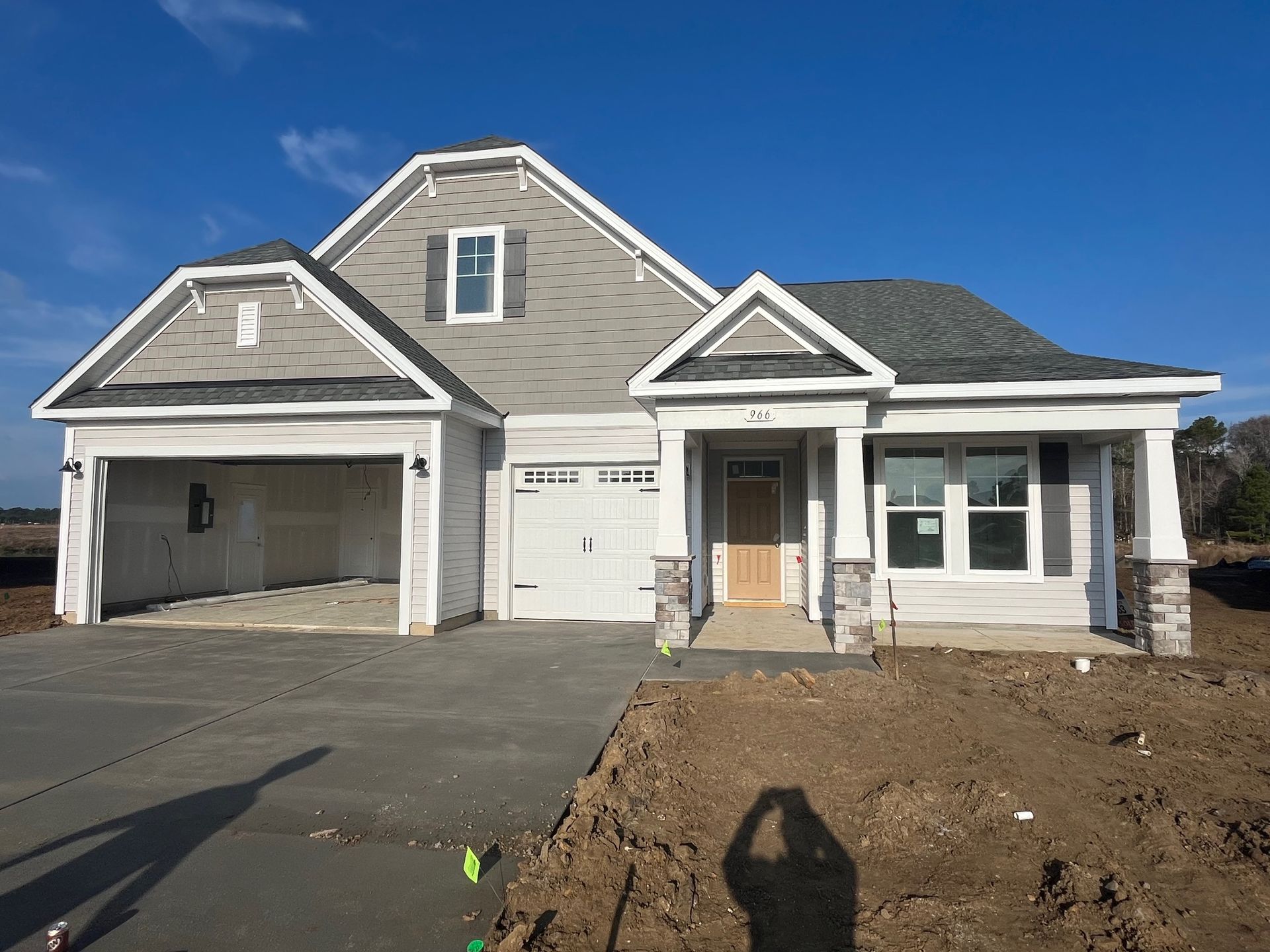 New house under construction with a light gray exterior, featuring a garage and front porch.