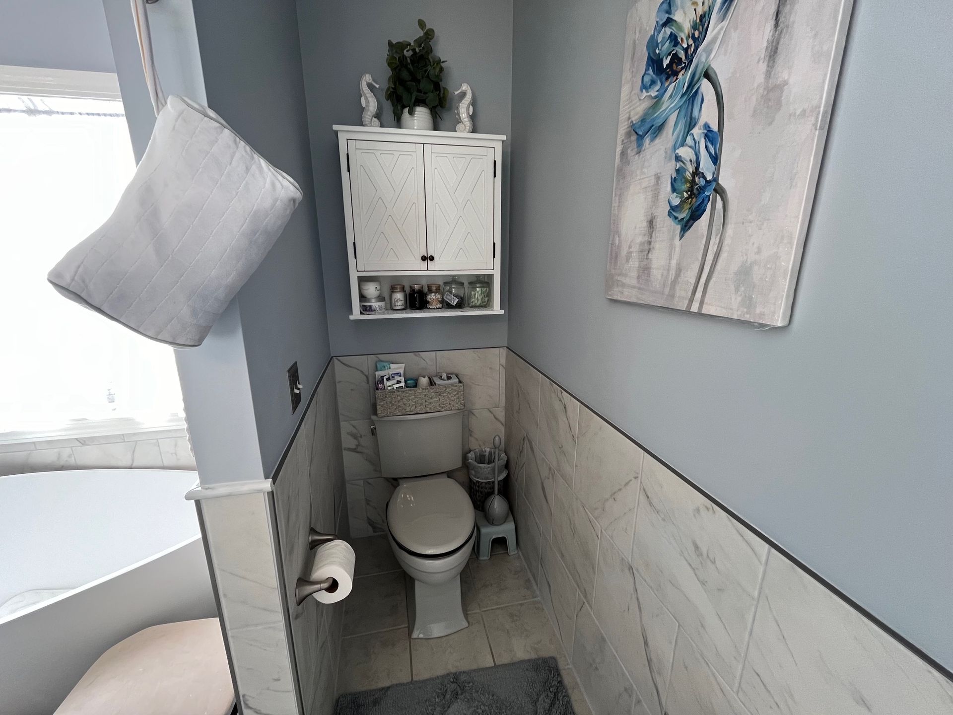 A small bathroom with a toilet, cabinet, and floral artwork. Gray and white color scheme.