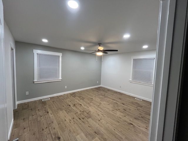 Empty bedroom with wood-look floor, gray walls, two windows with blinds, and ceiling fan.