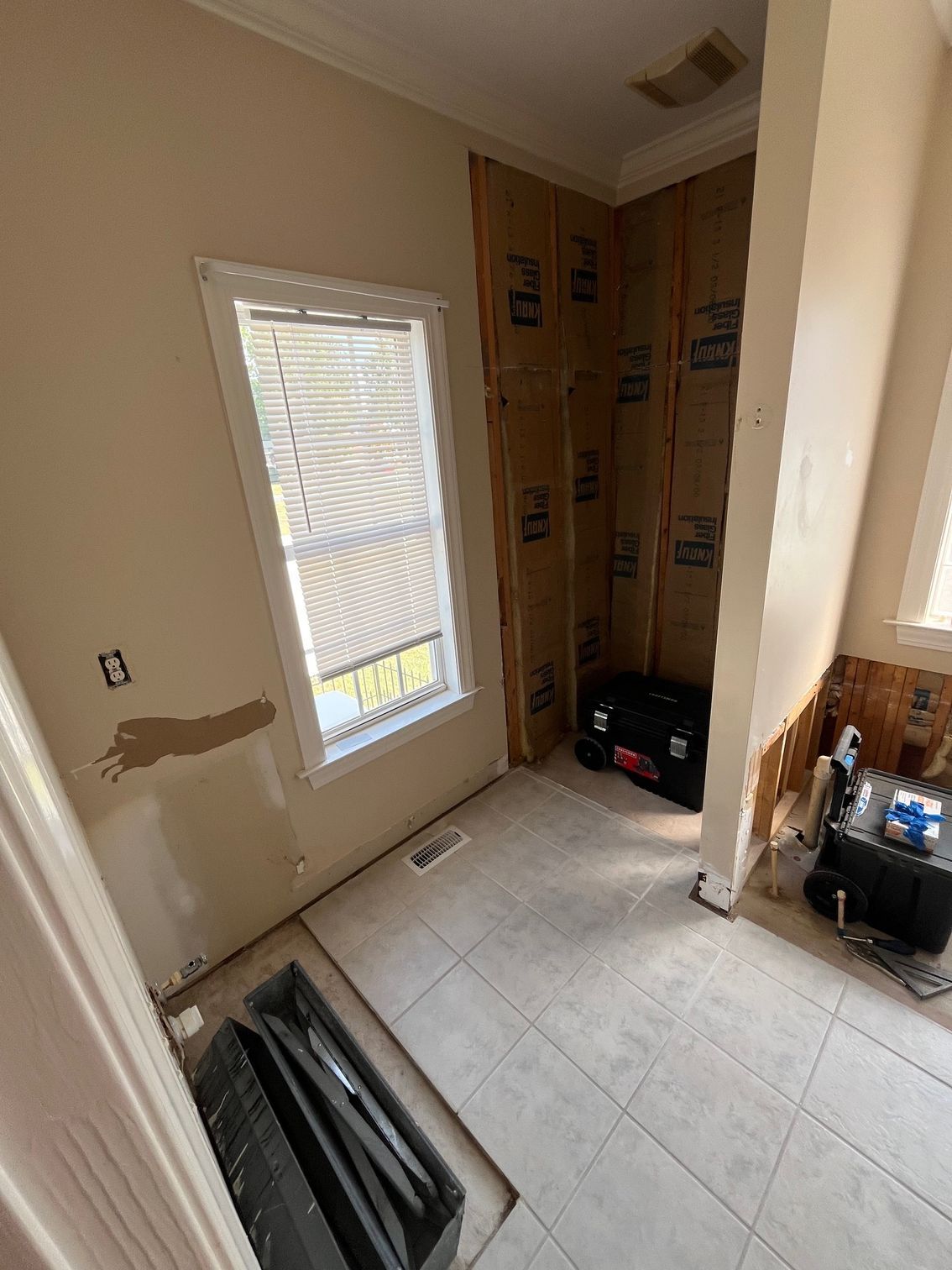 Bathroom under construction with exposed insulation, window with blinds, and tiled floor.