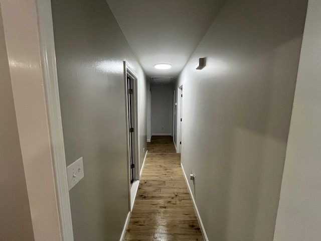 Narrow hallway with gray walls, wooden floor, and doors on either side. A skylight is in the ceiling.