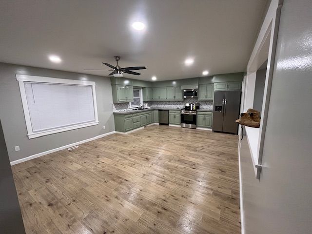 Spacious, open-concept kitchen with sage green cabinets, stainless steel appliances, and wood-look flooring.