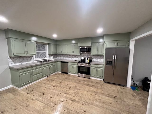 Kitchen with sage green cabinets, stainless steel appliances, and wood-look flooring.