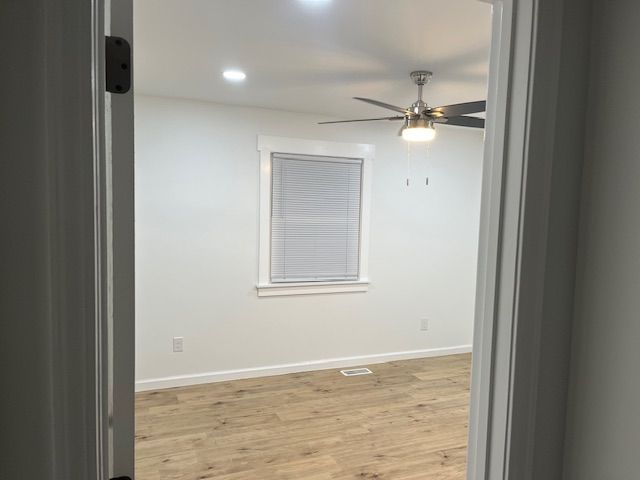 View through an open doorway into a bright, empty room with light wood floors and a window.