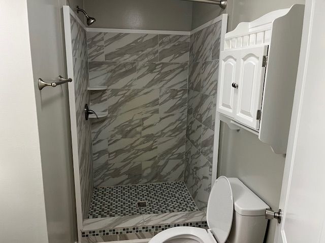 Bathroom with marble-look shower, mosaic floor, toilet, and white cabinet.