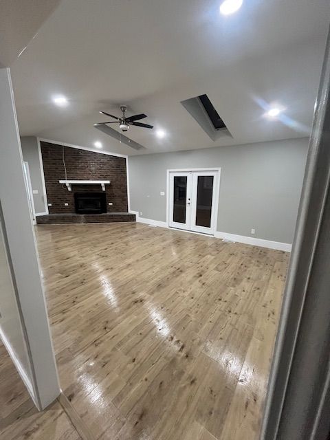 Empty living room with wood floors, brick fireplace, and double doors to outside.