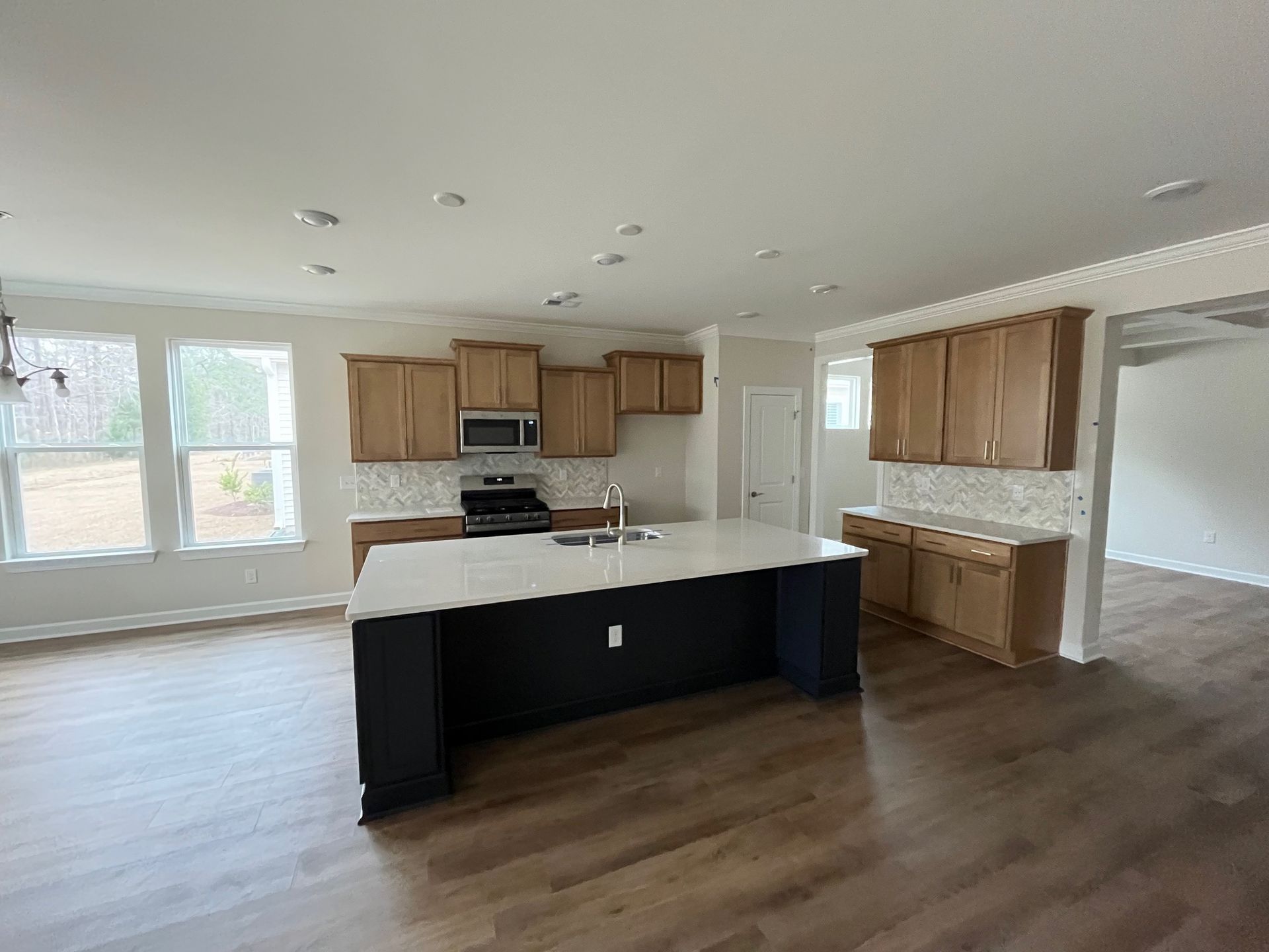 Kitchen with light wood cabinets, dark island, white countertops, and hardwood floors.