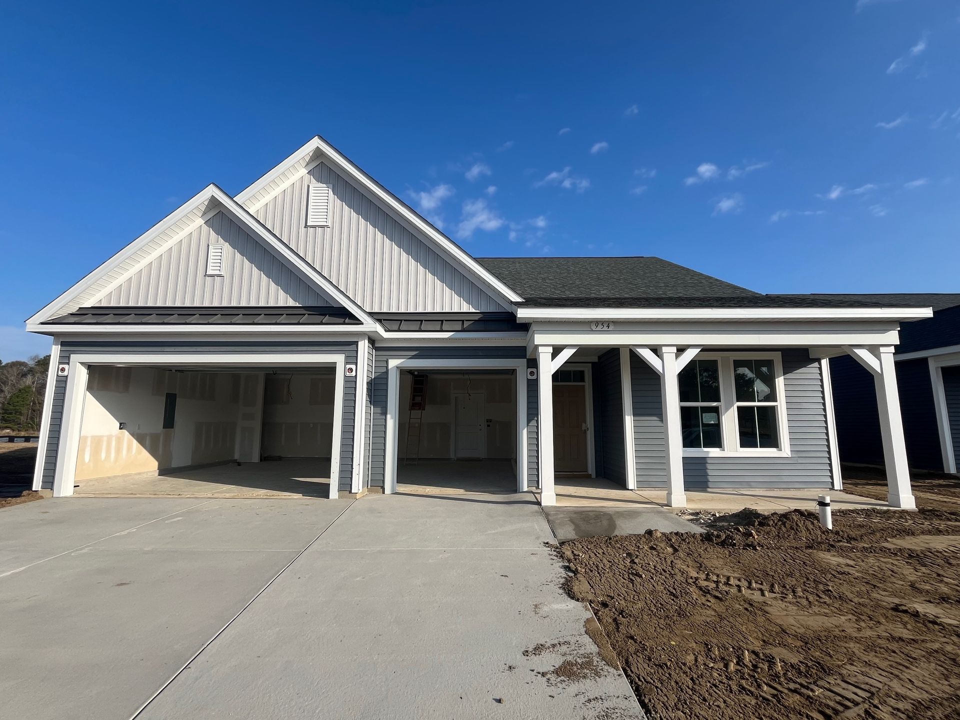 Exterior of a new, gray house with a two-car garage under a clear blue sky.