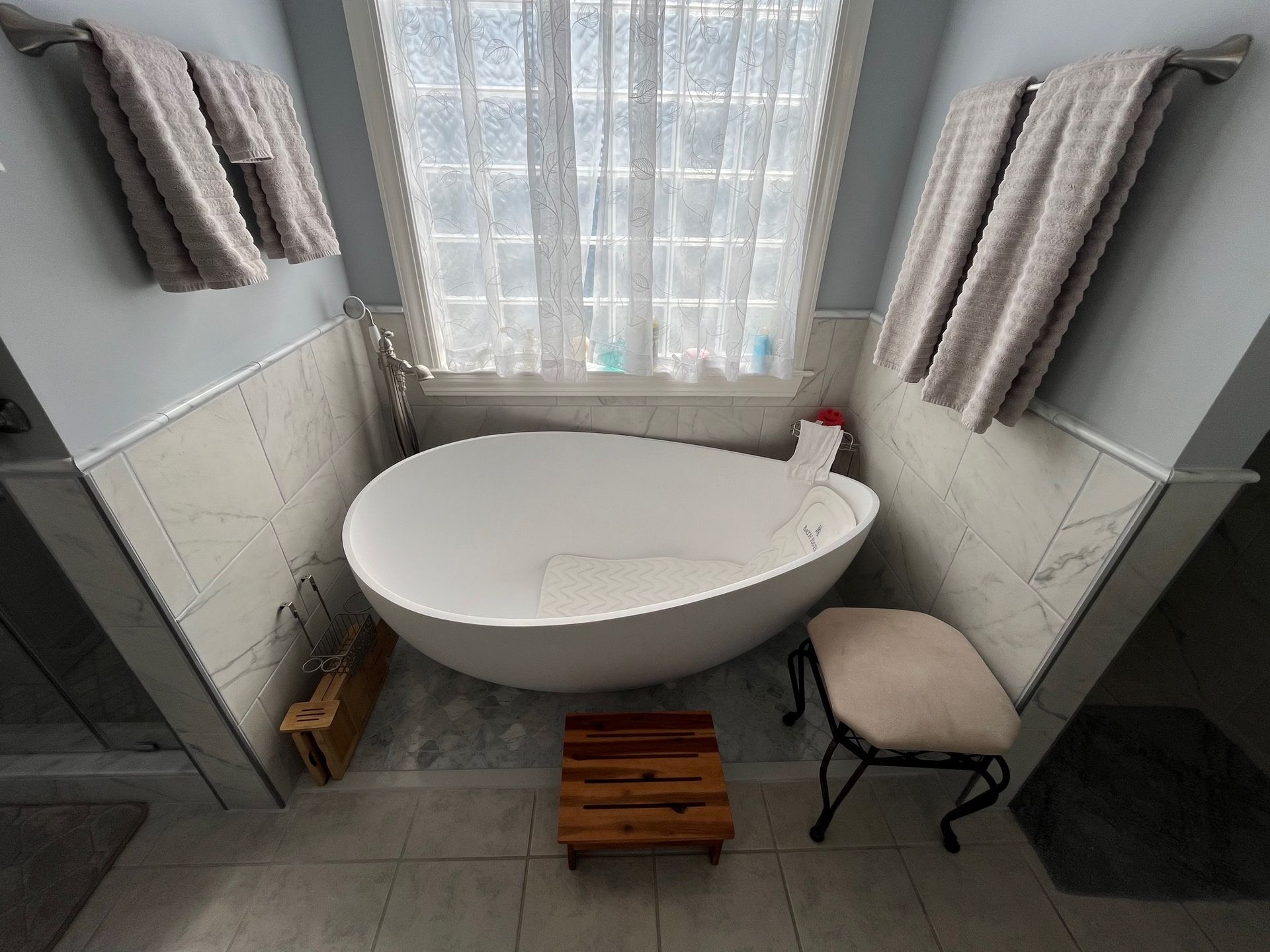 Bathroom with a white egg-shaped tub under a window, flanked by towel racks.