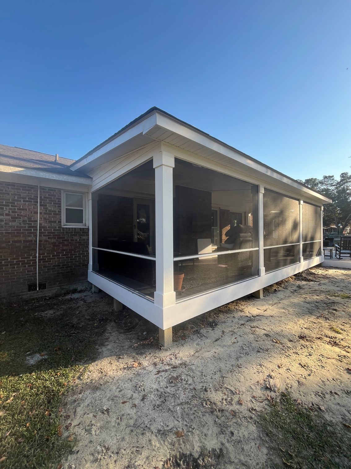 Concrete patio with a screened porch attached to a brick house. A bench and patio furniture sit on the patio.