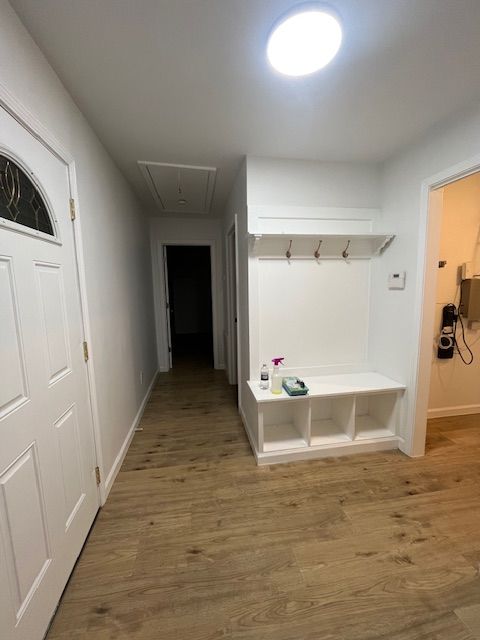 Hallway with white walls and wood-look flooring. White bench with hooks and storage. Bright overhead light.