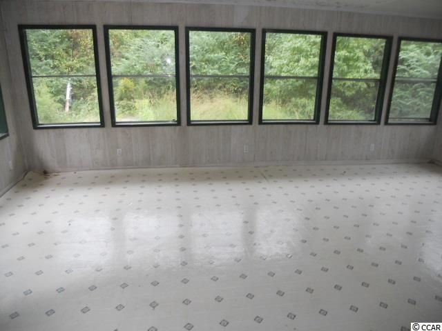 Sunroom with white panel walls, patterned floor, and large windows overlooking a green landscape.